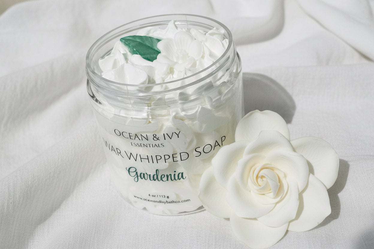 Clear container of Gardenia scented whipped soap with visible brand name on a light background