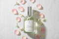 Clear room spray bottle with silver cap on a decorative surface with flowers and books.