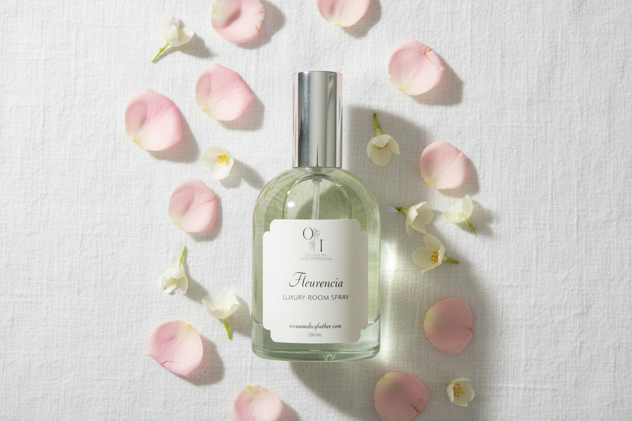 Clear room spray bottle with silver cap on a decorative surface with flowers and books.